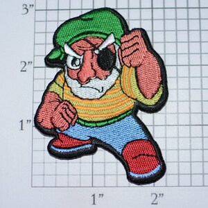 May include: Embroidered patch of a cartoon pirate with a green hat, an eyepatch, a striped shirt, and blue pants. The pirate is holding a fist up in the air.