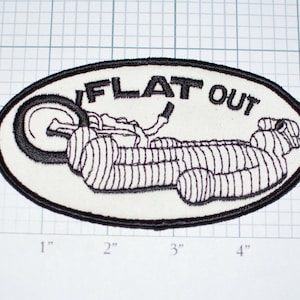 May include: White oval embroidered patch with black stitching. The patch depicts a motorcycle with the words "FLAT OUT" above it.