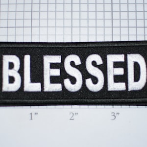 May include: Black fabric patch with white embroidered text that reads "BLESSED". The patch is approximately 1 inch tall and 3 inches wide.