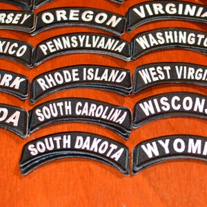 Puede incluir: Un conjunto de parches bordados en blanco y negro, cada uno con el nombre de un estado de EE. UU. en letras blancas arqueadas. Los estados incluyen Nueva Jersey, Oreg&oacute;n, Virginia, Nuevo M&eacute;xico, Pensilvania, Washington, Nueva York, Rhode Island, Virginia Occidental, Nevada, Carolina del Sur, Wisconsin, Dakota del Sur y Wyoming.
