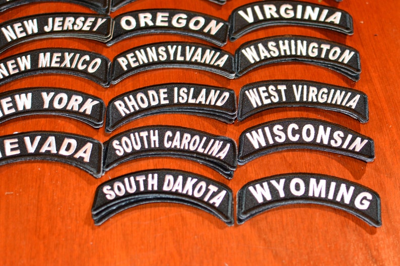 Puede incluir: Un conjunto de parches bordados en blanco y negro, cada uno con el nombre de un estado de EE. UU. en letras blancas arqueadas. Los estados incluyen Nueva Jersey, Oreg&oacute;n, Virginia, Nuevo M&eacute;xico, Pensilvania, Washington, Nueva York, Rhode Island, Virginia Occidental, Nevada, Carolina del Sur, Wisconsin, Dakota del Sur y Wyoming.