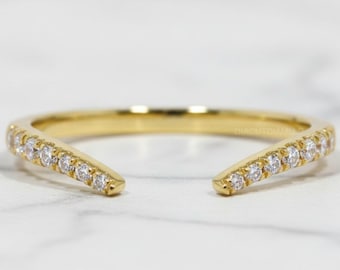 May include: A gold-colored open ring with a row of small, clear gemstones set along the top edges. The ring has a split design, with the ends curving away from each other.