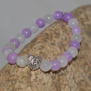 May include: A purple and white beaded bracelet with a silver heart charm featuring a wing design.