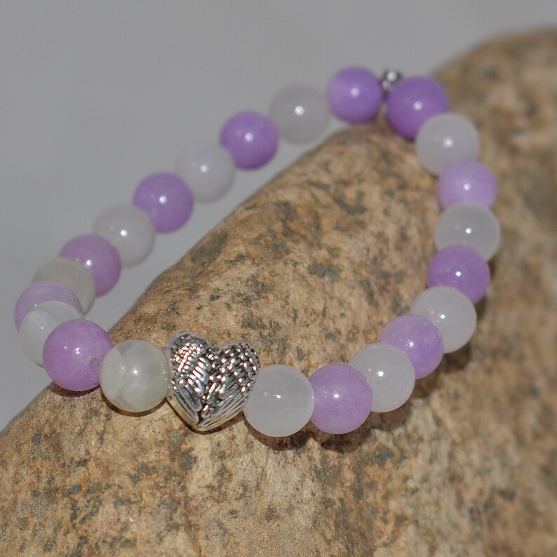 May include: A purple and white beaded bracelet with a silver heart charm featuring a wing design.