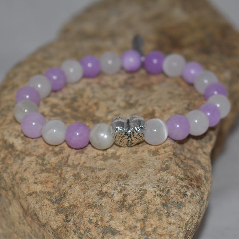 May include: A purple and white beaded bracelet with a silver charm in the shape of angel wings.