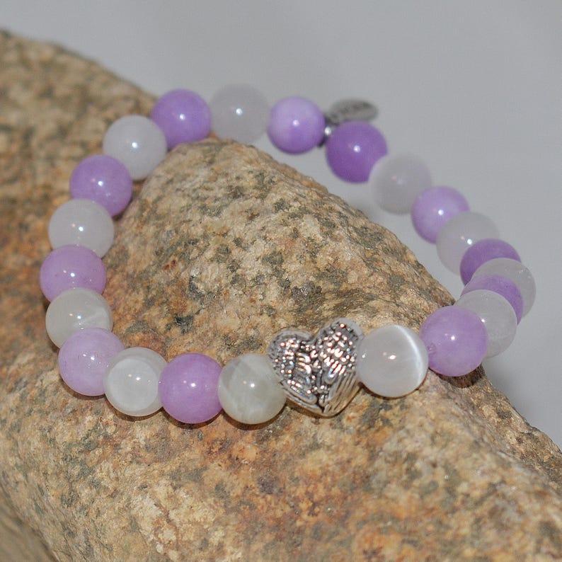 May include: A purple and white beaded bracelet with a silver heart charm featuring angel wings.