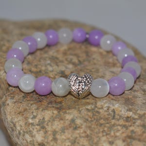 May include: A purple and white beaded bracelet with a silver heart charm featuring angel wings.