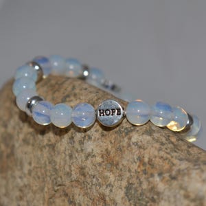May include: A white opal beaded bracelet with a silver charm that says "HOPE".