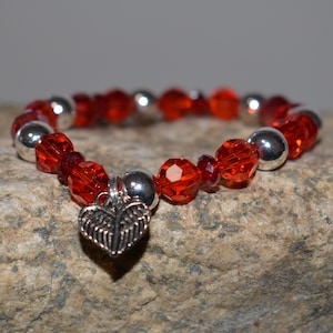 Puede incluir: Una pulsera de cuentas rojas con detalles plateados y un dije en forma de coraz&oacute;n. La pulsera presenta cuentas rojas facetadas intercaladas con cuentas plateadas. Un dije de coraz&oacute;n plateado con dise&ntilde;o de hojas cuelga.