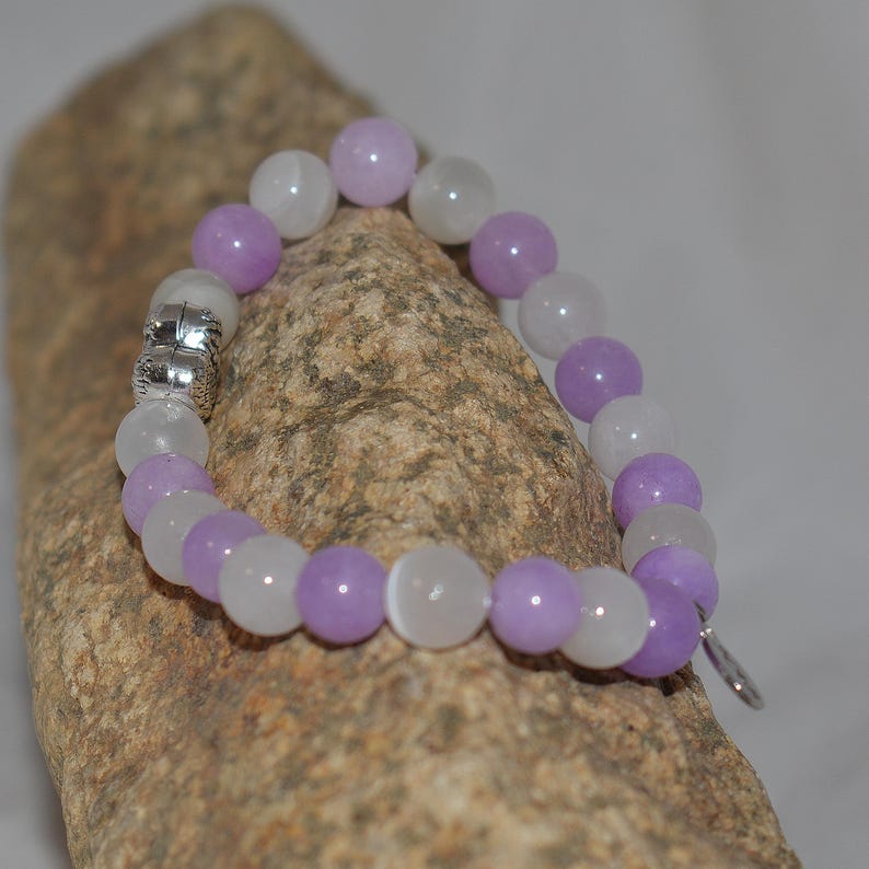 May include: A purple and white beaded bracelet with a silver clasp. The bracelet is made of round beads and is approximately 7 inches in length.