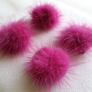 Pode incluir: Quatro pompons de pelo rosa sobre uma superfície branca.