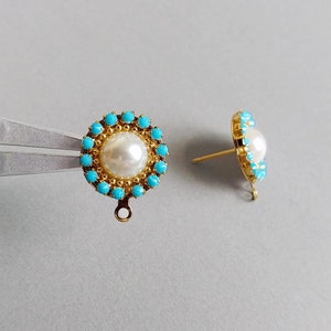 May include: Two gold-colored stud earrings. Each earring features a central white pearl surrounded by small turquoise-colored stones. The earrings have a floral design and a post for pierced ears. The earrings are shown on a light gray background.