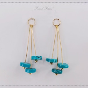 May include: Gold earrings with turquoise stones hanging from three gold wires. The earrings are on a white background with the text "Trend Tassel" above them.