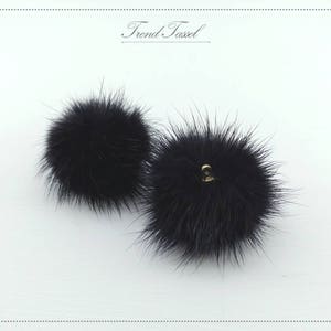 May include: Two black fluffy pom poms with a gold loop attachment.