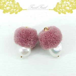 May include: A pair of pink fuzzy pom-pom earrings with a pearl accent. The earrings are attached to a gold hook.
