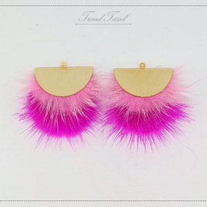 May include: A pair of pink and white faux fur earrings with gold metal half-circle accents. The earrings have a gold jump ring for hanging.