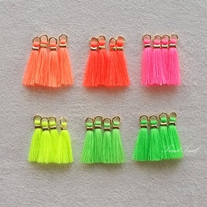 Könnte beinhalten: Set mit 20 Quasten in Neonfarben mit goldenen Ringen. Die Quasten sind in vier Farben: Pink, Orange, Grün und Gelb.