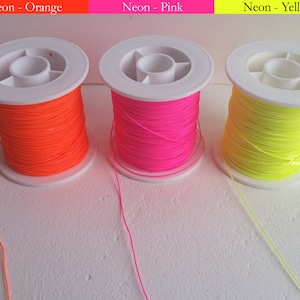Puede incluir: Tres carretes de hilo neón en naranja, rosa y amarillo. Cada carrete está enrollado en una bobina de plástico blanco. El texto "Neon - Orange", "Neon - Pink" y "Neon - Yellow" se muestra encima de cada carrete.