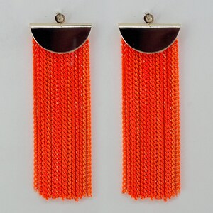 May include: A pair of orange tassel earrings with a silver half-circle top.