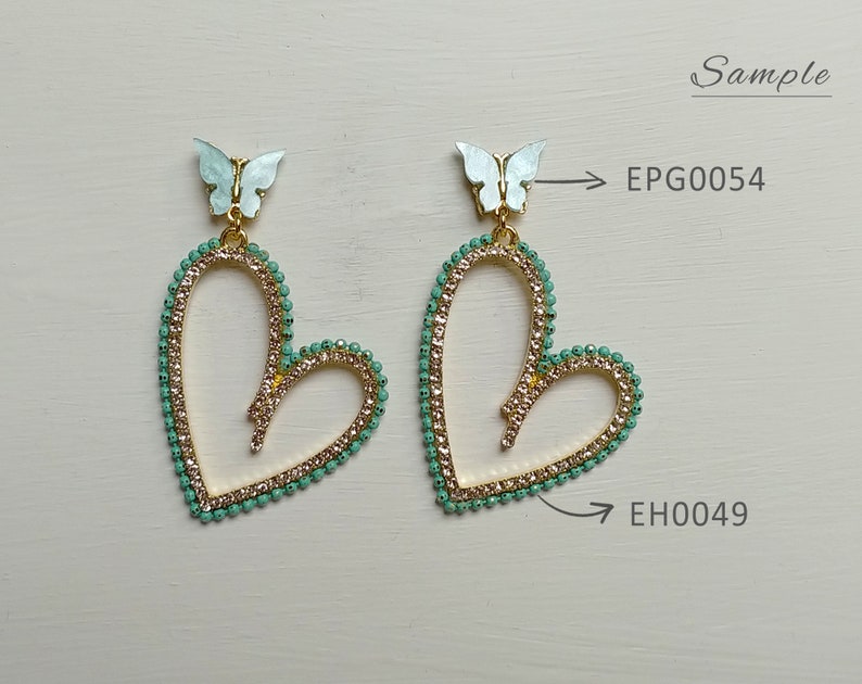 May include: A pair of heart-shaped earrings with a gold-colored frame, adorned with small, light green beads and clear crystals. Each earring features a light blue butterfly at the top. The earrings are labeled "EPG0054" and "EH0049".