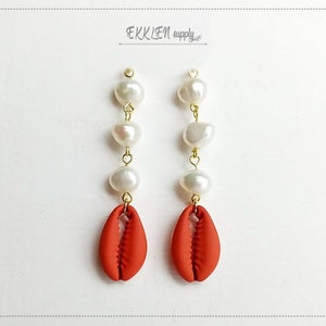 May include: A pair of earrings with a red shell charm and a chain of white pearls.