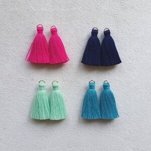 Peut inclure: Quatre paires de pompons colorés avec des anneaux dorés. Les pompons sont roses, bleus, vert clair et turquoise.