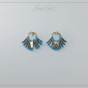 May include: A pair of gold hoop earrings with turquoise blue fringe. The earrings are small and delicate.