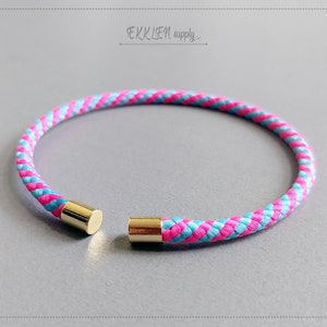 Könnte beinhalten: Ein geflochtenes Armband mit einem rosa und blauen Muster. Das Armband hat goldfarbene Metallenden. Der Text "EKKLEN supply..." befindet sich in der oberen rechten Ecke.