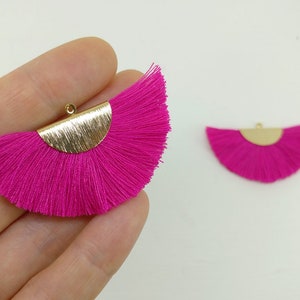 May include: Two pink tassel earrings with gold metal accents. The earrings are shaped like a half-circle and have a fringe of pink tassels.