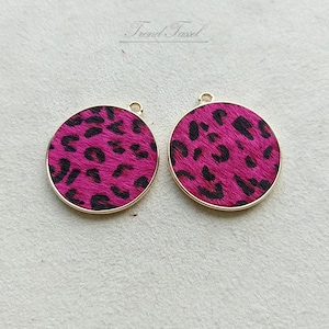 May include: Two round pink and black leopard print charms with gold metal frames.
