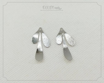 May include: Two silver-colored metal leaf-shaped pendants. Each pendant has three leaf-like sections and a small hole at the top for hanging. The pendants have a brushed metal texture and are displayed on a light-colored surface.