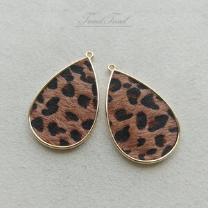 May include: Two teardrop-shaped earring pendants with a gold-colored border. The interior features a brown and black leopard print design. The text "Trend.Tassel" is visible at the top.