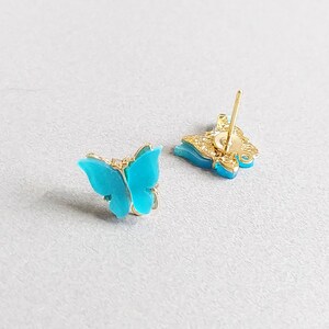 May include: A pair of butterfly stud earrings. The butterfly wings are a vibrant turquoise color, set in a gold-colored metal frame. The earrings have a post backing for pierced ears.