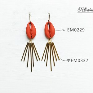 May include: A pair of dangle earrings featuring a terracotta-colored shell-shaped bead suspended from a gold-tone hook. Below the shell, a cluster of gold-tone rods radiates outward. The earrings are labeled EM0229 and EM0337.