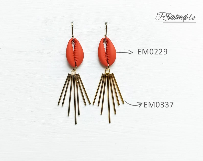 May include: A pair of dangle earrings featuring a terracotta-colored shell-shaped bead suspended from a gold-tone hook. Below the shell, a cluster of gold-tone rods radiates outward. The earrings are labeled EM0229 and EM0337.