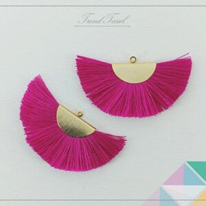 May include: Two pink tassel fringe trim pieces with gold metal half-circle accents. The tassels are arranged in a fan shape.