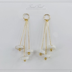 May include: A pair of gold-coloured dangle earrings. Each earring has a small gold ring at the top, with three gold wires descending to hold white, disc-shaped beads and small gold spheres. The earrings are set against a white background.