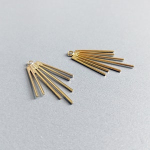 May include: Two gold-colored metal earring components. Each component features a small loop at the top and a fan-like arrangement of thin, straight bars radiating outwards. The components are displayed against a light gray background.