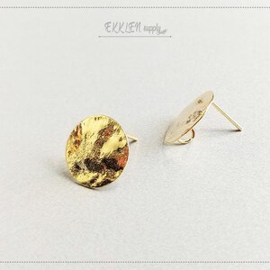May include: Two gold-colored stud earrings. Each earring features a hammered, textured, circular design. The earrings have a post and backing for secure wear. The earrings are displayed on a light gray surface.