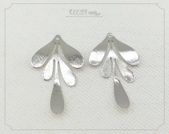 May include: Two silver-colored leaf-shaped pendants with a brushed metal finish. Each pendant has a small hole at the top for stringing and a stylized leaf design. The pendants are likely for jewelry making or crafting.