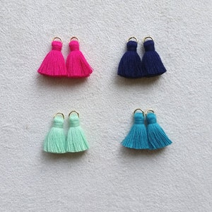 Może przedstawiać: Cztery pary małych frędzli w różnych kolorach: różowym, niebieskim, jasnozielonym i turkusowym. Każda frędzla ma złoty pierścień na górze.