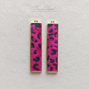 Pode incluir: Dois pingentes de barra de metal dourado com um design de estampa de leopardo rosa e preto.