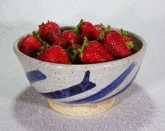 May include: A white ceramic bowl with blue stripes and a speckled glaze, filled with fresh red strawberries.