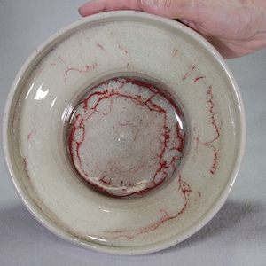 以下が含まれることがあります： 赤い釉薬のデザインが施された白い陶器のボウル。ボウルは広い縁と深い中心部を持っています。