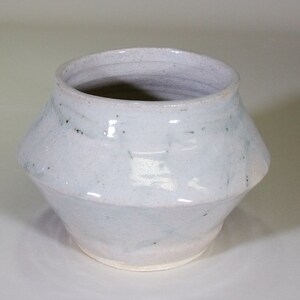 Peut inclure: Un pot en céramique blanche avec une base arrondie et une large ouverture. Le pot a une surface légèrement texturée et un glaçage subtil.