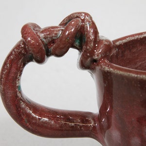 Small maroon stoneware cup with entwined handle.