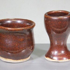 May include: Two brown ceramic cups, one with a rounded shape and the other with a flared base. Both cups have a speckled glaze.