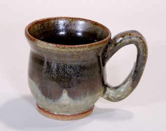 Pode incluir: Uma caneca de cerâmica marrom e verde com corpo arredondado e alça. A caneca tem um esmalte salpicado com uma faixa verde claro e branca ao redor da base.