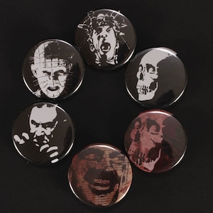 Könnte beinhalten: Eine Sammlung von sechs schwarzen und weißen Horror-Button-Pins. Die Pins zeigen verschiedene grafische Illustrationen von Gesichtern und Schädeln. Die Pins sind kreisförmig auf schwarzem Hintergrund angeordnet.
