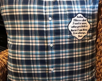 May include: A square throw cushion crafted from a blue, white, and black plaid button-down shirt. The cushion features a central vertical placket with three white buttons and a chest pocket displaying an embroidered patch with the text: Kellen, This is a shirt I used to wear, when you hold it know I am there. Love always, Dad.